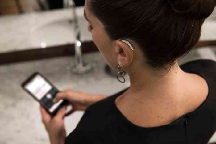 A woman wearing a BTE hearing aid is checking her device's app
