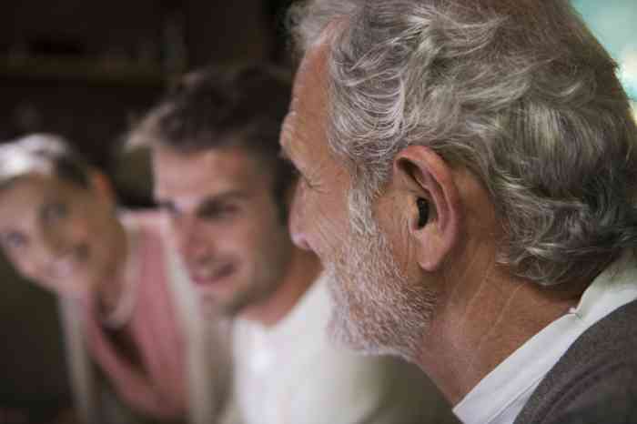 A Grandpa wearing hearing aids teaches to his Grandson how to go skateboarding
