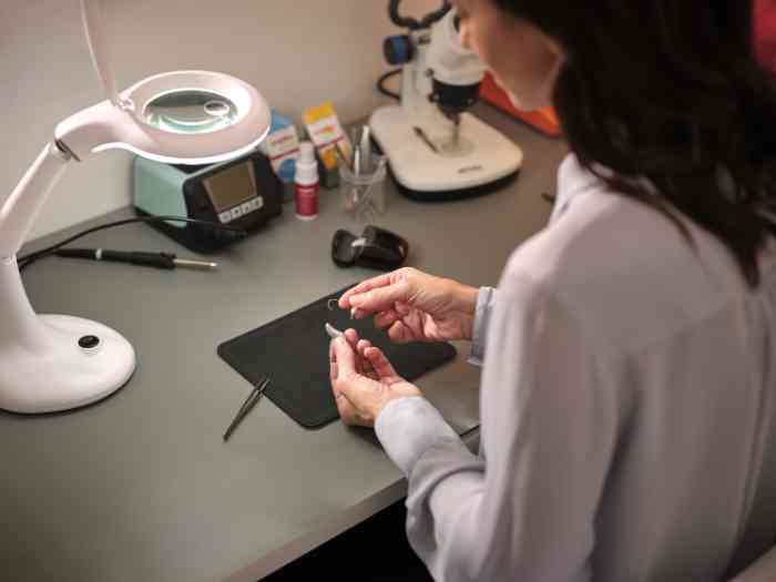audiologiste en laboratoire travaillant sur un appareil auditif, sans blouse.