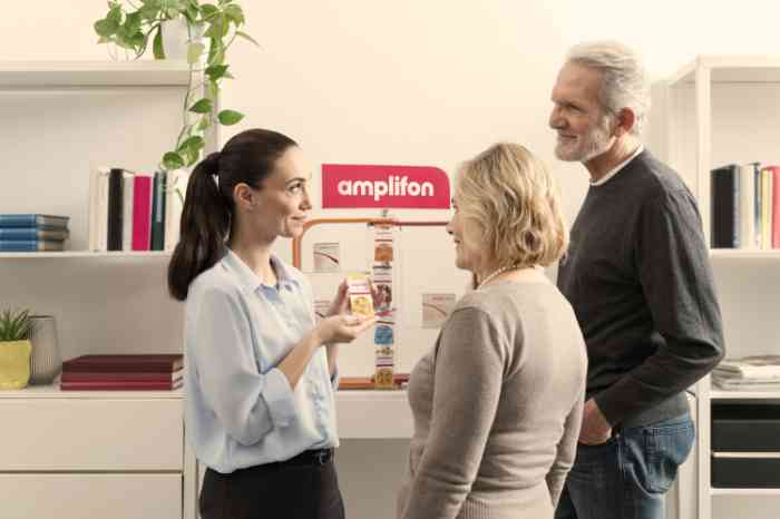 Audiologiste montrant des piles pour aides auditives Amplifon à deux clients en magasin.
