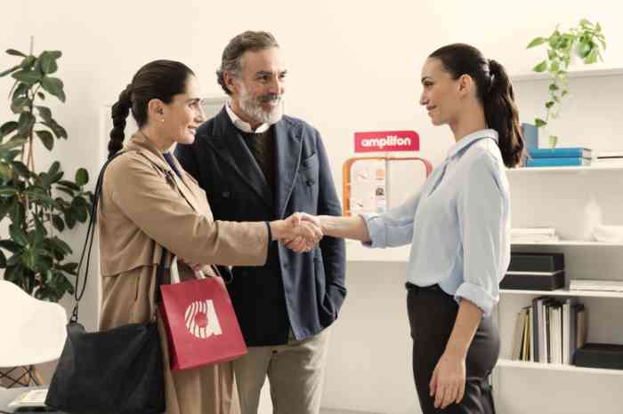 Audiologist in blue shirt shaking hands with a smiling couple in an Amplifon store.
