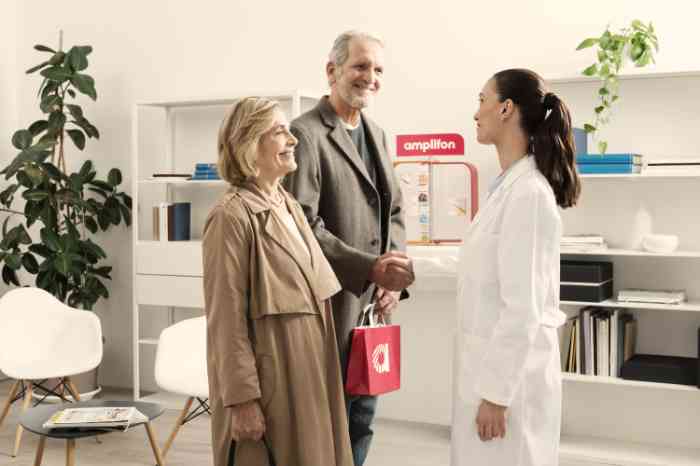 Audiologist in lab coat shaking hands with a happy elderly couple in an Amplifon store.