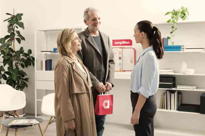 Audiologist in blue shirt talking with an elderly couple in an Amplifon store.