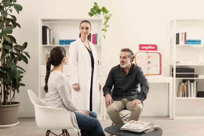 Audiologist in lab coat standing and talking with two seated clients in an Amplifon store.