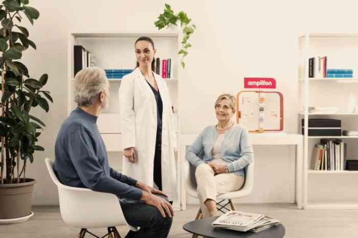 Audiologist in lab coat standing and talking with two seated clients in an Amplifon store.