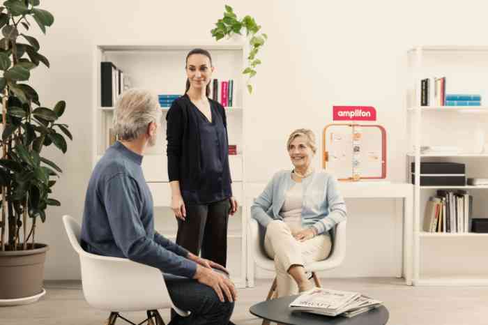 Audiologist standing and talking with two seated clients in an Amplifon store.
