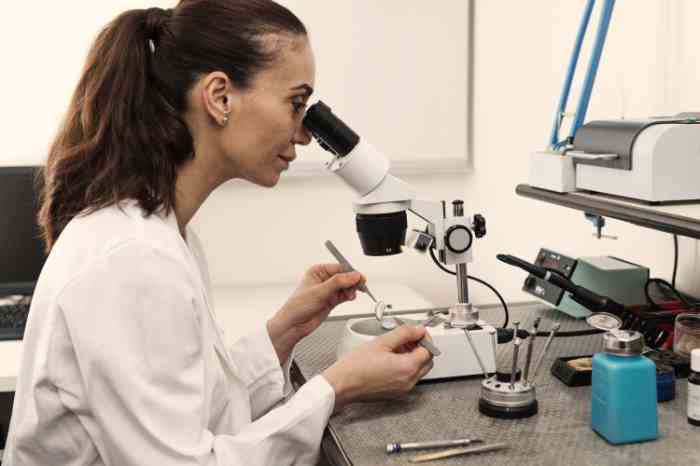 An audiologist in a lab coat examines hearing aids under a microscope