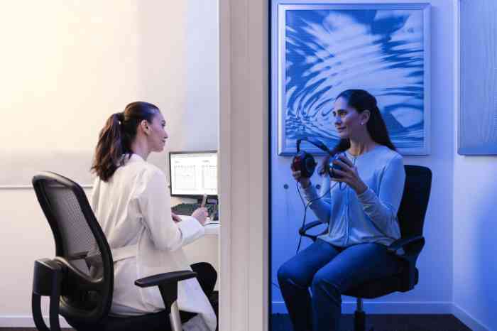 An audiologist in a lab coat is about to conduct a hearing test on a woman