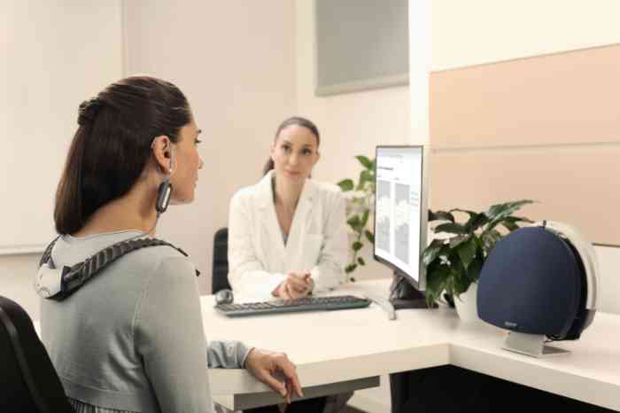 A woman wearing a hearing test device while an Amplifon professional analyzes the results.