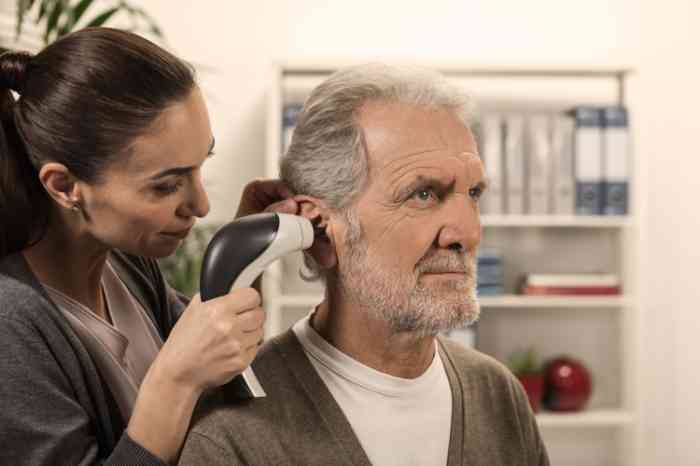 Audiologist without a coat examines an elderly man’s ear with a video otoscope.
