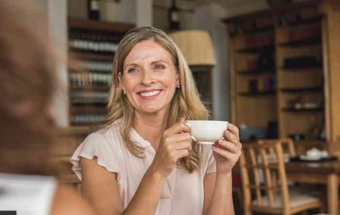 woman smiling in a café with a cup in hand.