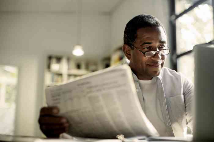 A man works on a PC and reads a newspaper, listening to the world around