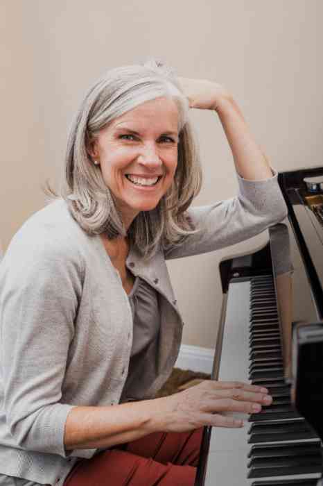 A woman is smiling next to a piano
