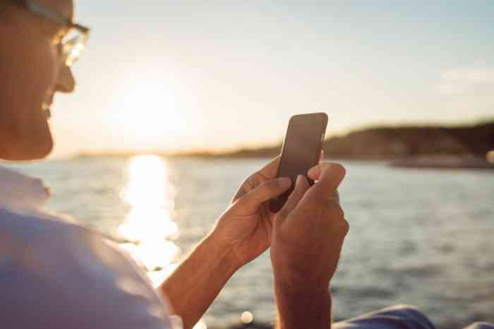 Homme avec téléphone à la main sur la plage au coucher du soleil